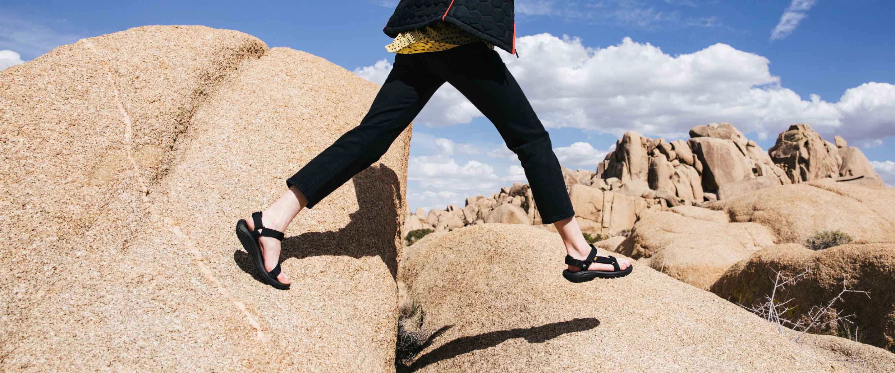 Woman walking over large rocks wearing Teva sandals.